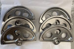 Eight metallic curved parts with circular cutouts arranged on a surface.